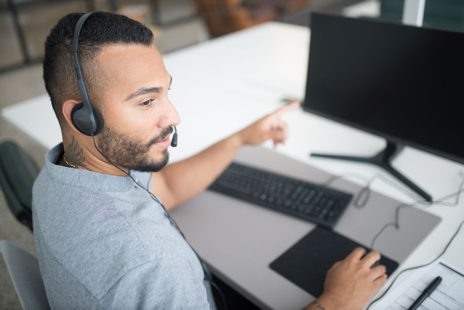 Agente de atendimento ao cliente usando um computador e fones de ouvido em um ambiente de escritório moderno.