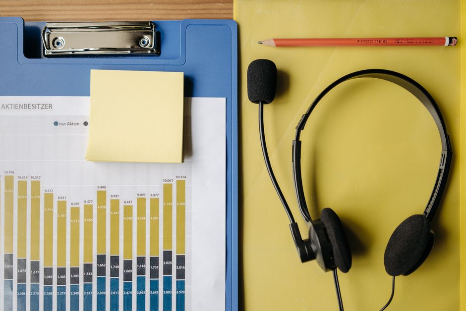 Visão de cima de itens de escritório, incluindo um gráfico, fones de ouvido e material de papelaria em uma mesa.