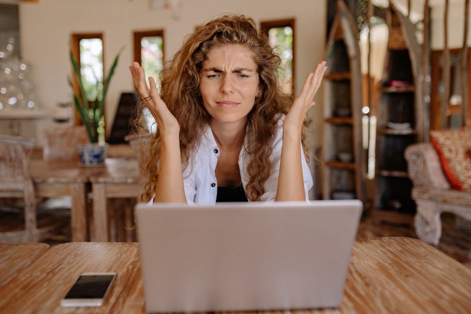 Uma mulher frustrada com seu laptop enquanto trabalha remotamente em casa, expressando estresse.