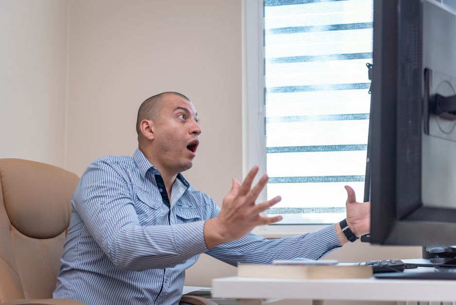 Homem no escritório chocado com a tela do computador.