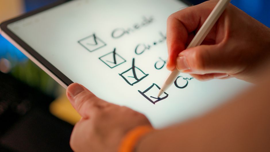 Close-up de uma lista de verificação digital sendo marcada em um tablet com uma caneta stylus.