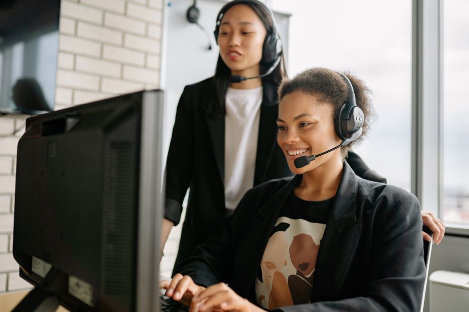 Duas mulheres com fones de ouvido envolvidas em atendimento ao cliente em um computador em um escritório iluminado.